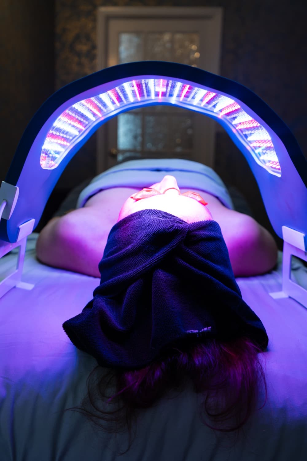 Guest resting under the arched LED light therapy panel after a facial in the treatment room at LNO Boutique in Centennial, Denver