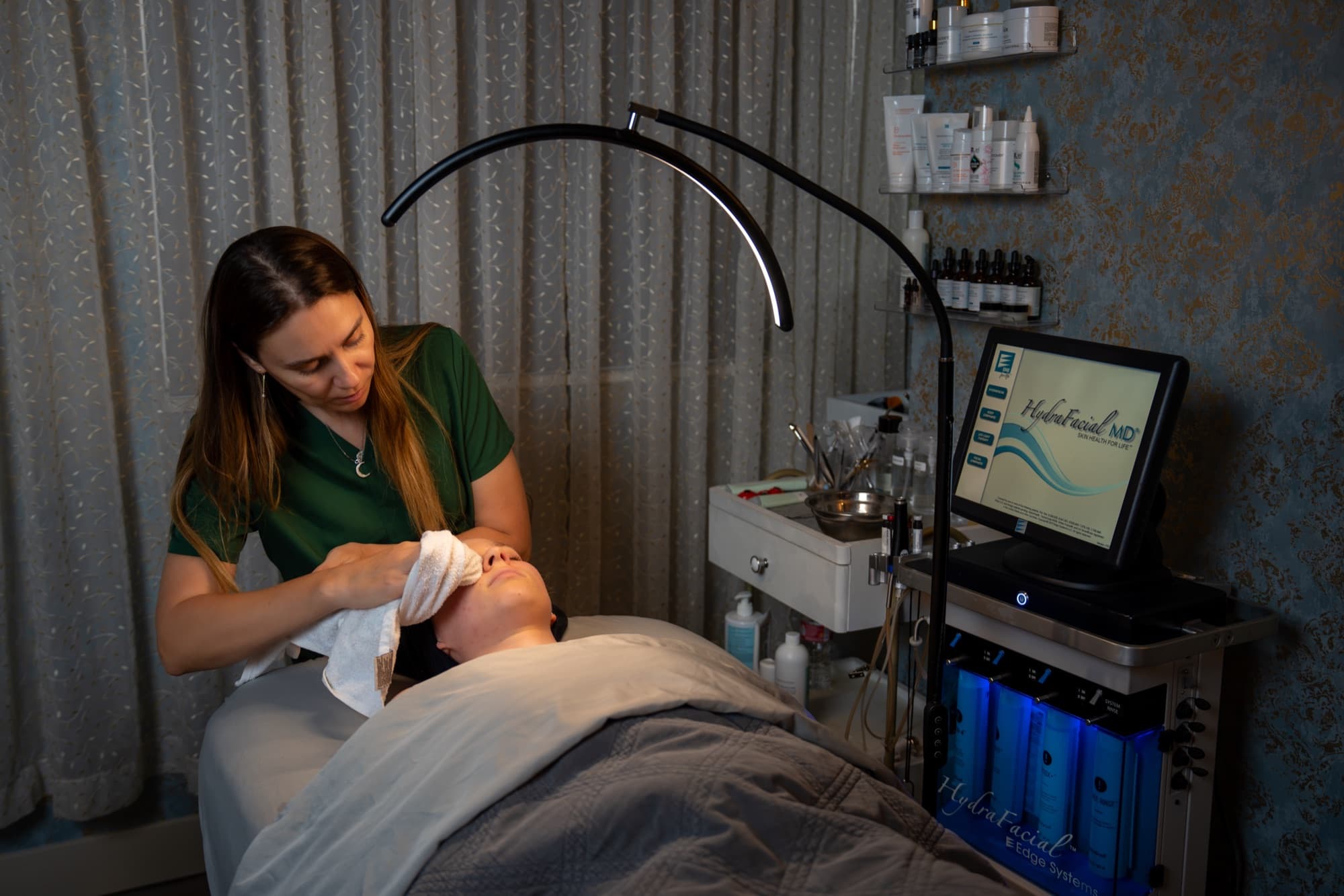 Esthetician giving a HydraFacial with the HydraFacial MD device beneath the arc lamp at LNO Boutique in Centennial, Denver